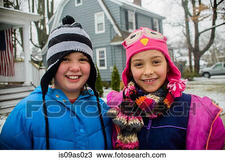 Stock Image - Portrait of two girls wearing knitted hats in snowy garden. Fotosearch