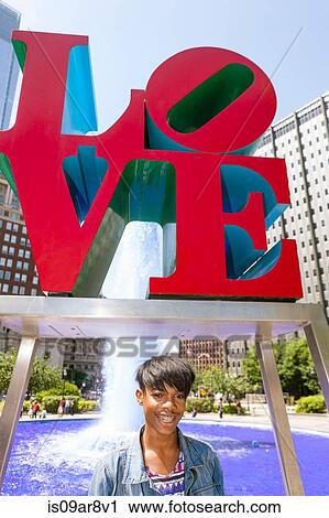 Stock Image - Portrait of young man in front of red Love sign, Philadelphia, Pennsylvania, USA. Fotosearch