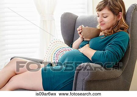 Pregnant woman drinking bowl of soup on living room armchair View Large Photo Image Stock Photo - Pregnant woman drinking bowl of soup on living room armchair. Fotosearch