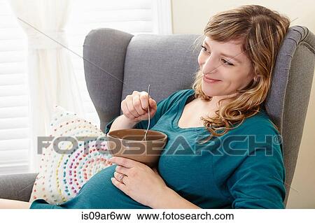 Pregnant woman eating bowl of soup on living room armchair View Large Photo Image Stock Photo - Pregnant woman eating bowl of soup on living room armchair. Fotosearch