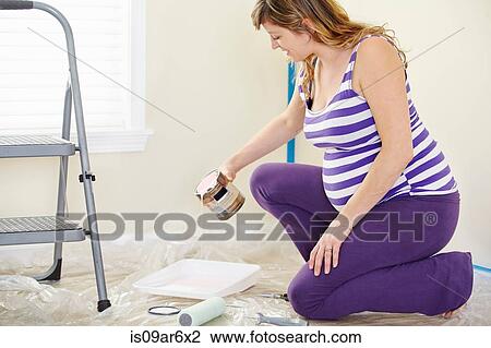 Stock Image - Pregnant woman pouring pink paint to decorate nursery. Fotosearch