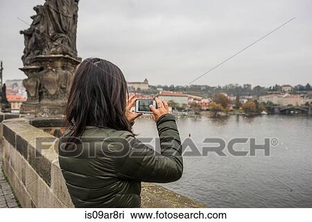 Stock Image - Rear view of woman using smartphone on Charles Bridge, Prague. Fotosearch