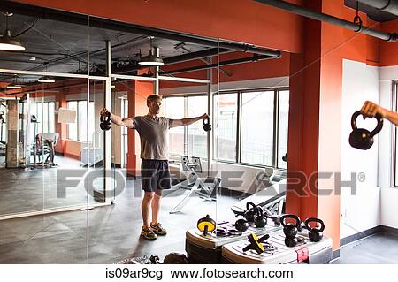 Reflection of mid adult man looking at himself in gym mirror training with kettle bells View Large Photo Image Stock Image - Reflection of mid adult man looking at himself in gym mirror training with kettle bells. Fotosearch