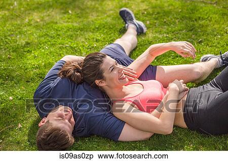 Stock Photography - Romantic young sporty couple lying on park grass. Fotosearch