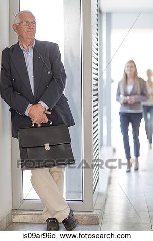 Picture - Senior businessman leaning against hotel corridor wall. Fotosearch