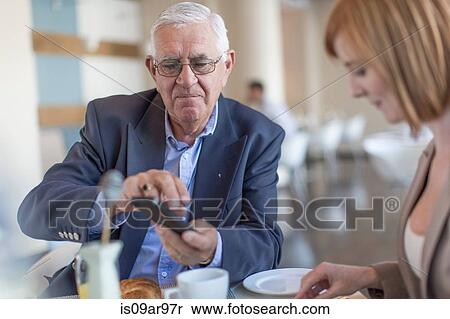 Stock Photography - Senior businessman smartphone texting at breakfast table in hotel restaurant. Fotosearch