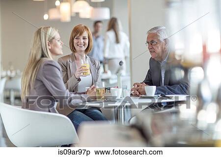 Stock Photography - Senior businessman talking to team at breakfast table in hotel restaurant. Fotosearch