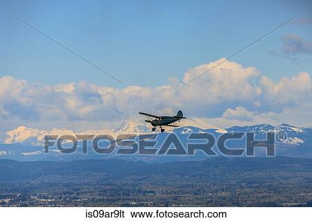 Silhouetted bi-plane flying above snow capped mountainous landscape View Large Photo Image Stock Photograph - Silhouetted bi-plane flying above snow capped mountainous landscape. Fotosearch