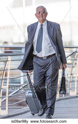 Smiling senior businessman leaving hotel with wheeled suitcase View Large Photo Image Stock Photo - Smiling senior businessman leaving hotel with wheeled suitcase. Fotosearch