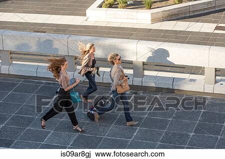 Three adult women running across elevated walkway View Large Photo Image Stock Image - Three adult women running across elevated walkway. Fotosearch