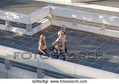 Stock Image - Three adult women walking across elevated walkway. Fotosearch