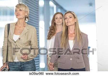 Stock Image - Three determined businesswomen walking in hotel corridor. Fotosearch