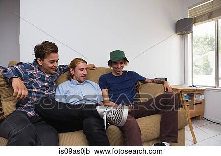 Three young men sitting on sofa, looking at smartphone View Large Photo Image Stock Image - Three young men sitting on sofa, looking at smartphone. Fotosearch