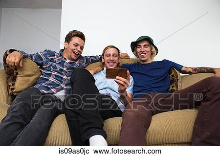 Three young men sitting on sofa, looking at smartphone View Large Photo Image Stock Image - Three young men sitting on sofa, looking at smartphone. Fotosearch