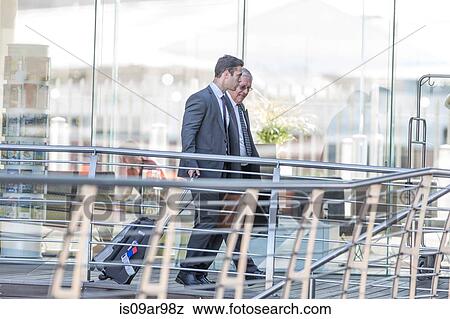 Two businessmen leaving hotel with wheeled suitcases View Large Photo Image Stock Photo - Two businessmen leaving hotel with wheeled suitcases. Fotosearch