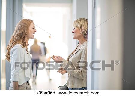 Stock Image - Two businesswomen chatting in hotel corridor. Fotosearch