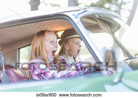Stock Image - Two young girls driving car, looking scared. Fotosearch