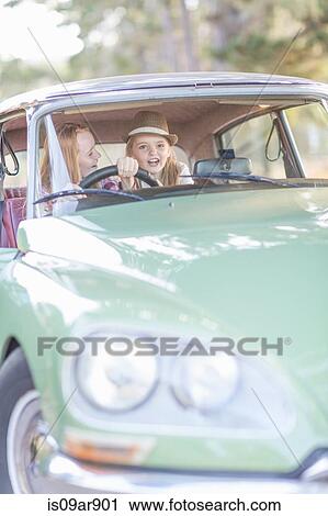 Stock Image - Two young girls in driving seat of car. Fotosearch