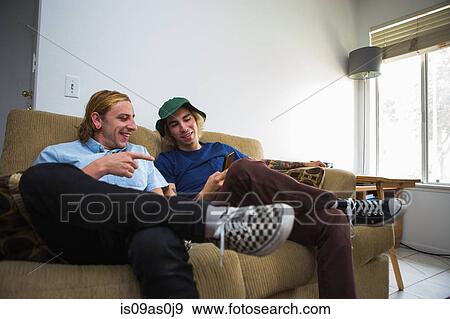 Stock Photo - Two young men sitting on sofa, looking at smartphone. Fotosearch