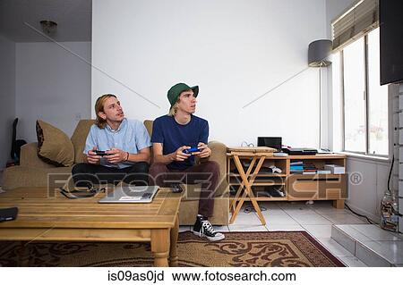 Two young men sitting on sofa, playing video game View Large Photo Image Stock Image - Two young men sitting on sofa, playing video game. Fotosearch