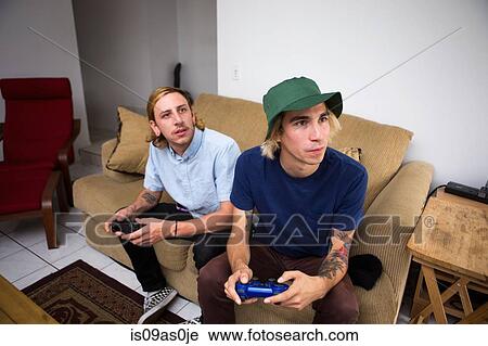 Two young men sitting on sofa, playing video game View Large Photo Image Stock Image - Two young men sitting on sofa, playing video game. Fotosearch