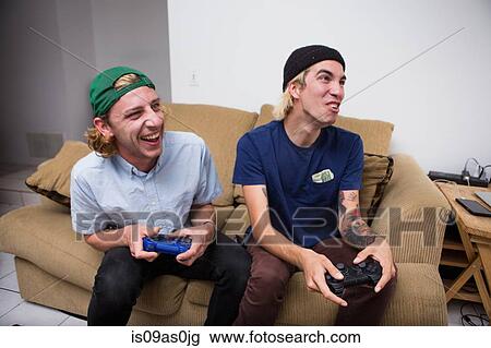 Two young men sitting on sofa, playing video game View Large Photo Image Stock Image - Two young men sitting on sofa, playing video game. Fotosearch