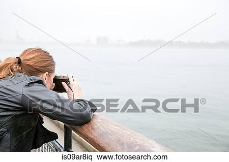 Stock Photography - Woman taking photograph from seawall, New York, New York, USA. Fotosearch