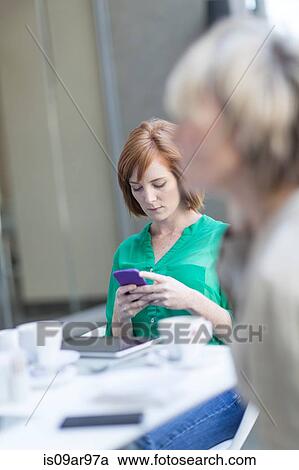 Stock Image - Young businesswomen reading smartphone texts on hotel terrace. Fotosearch
