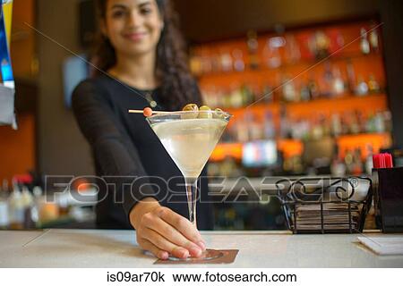 Stock Image - Young female bartender handing cocktail on counter of cocktail bar. Fotosearch