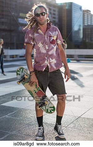 Young man holding skateboard, portrait View Large Photo Image Stock Image - Young man holding skateboard, portrait. Fotosearch