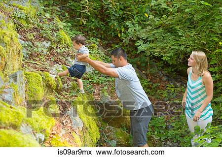 Stock Photo - Young man lifting toddler son onto rocks in park. Fotosearch