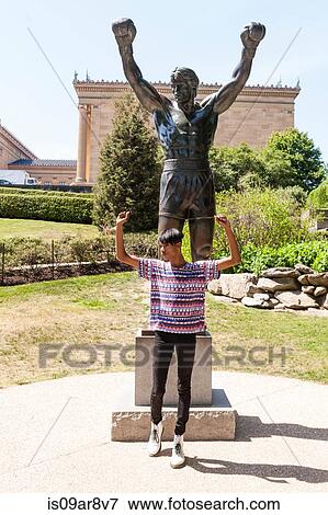 Stock Photo - Young man mimicking pose in front of park statue, Philadelphia, Pennsylvania, USA. Fotosearch