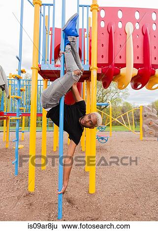 Stock Photograph - Young man upside down on pole in playground. Fotosearch