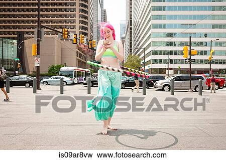 Young woman hoola hooping whilst reading smartphone text, Philadelphia, Pennsylvania, USA View Large Photo Image Stock Photo - Young woman hoola hooping whilst reading smartphone text, Philadelphia, Pennsylvania, USA. Fotosearch