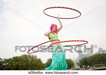 Stock Photograph - Young woman with pink hair hoola hooping in park, Philadelphia, Pennsylvania, USA. Fotosearch