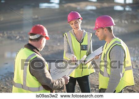 Stock Image - Architect and builders pointing to blueprint on construction site. Fotosearch