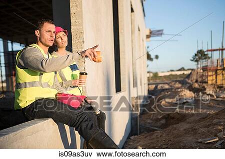 Stock Photo - Builder and architect pointing and looking out from window frame on construction site. Fotosearch