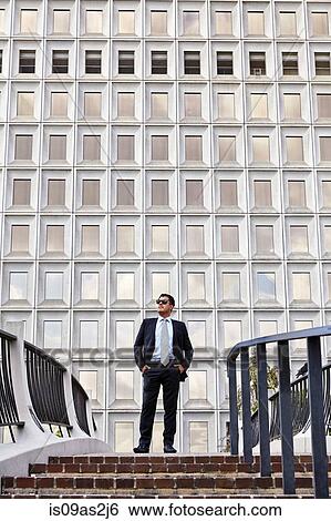 Stock Photograph - Business man standing at the top of stairway, wearing sunglasses, hands in pockets, looking away. Fotosearch
