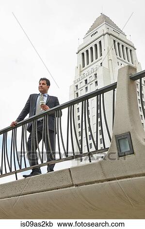 Stock Image - Business man standing on walkway holding coffee, Los Angeles City Hall, California, USA. Fotosearch