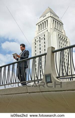 Business man standing on walkway looking at digital tablet, Los Angeles City Hall, California, USA View Large Photo Image Stock Image - Business man standing on walkway looking at digital tablet, Los Angeles City Hall, California, USA. Fotosearch