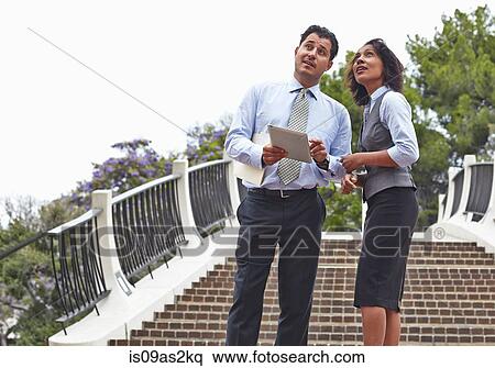 Stock Photography - Business people standing in front of stairway holding digital tablet, looking up. Fotosearch