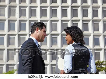 Stock Image - Business people standing talking face to face, holding paperwork, waist up. Fotosearch