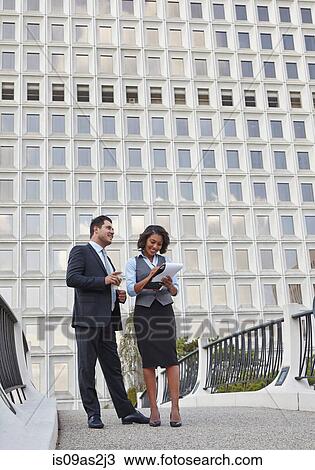 Stock Image - Business people standing talking holding paperwork. Fotosearch