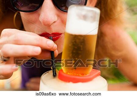 Picture - Close up of mid adult woman drinking beer with drinking straw. Fotosearch