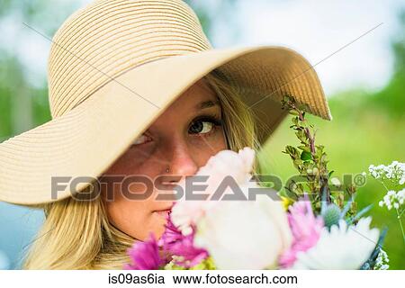 Stock Image - Close up portrait of young woman with bunch of flowers and wearing straw hat. Fotosearch