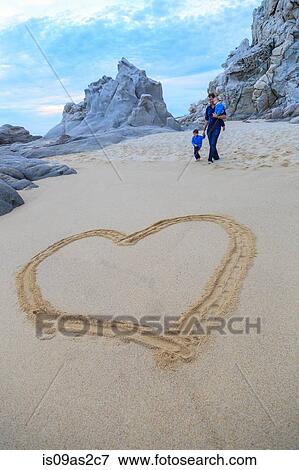 Stock Photo - Father and sons walking on beach, heart shape in foreground. Fotosearch