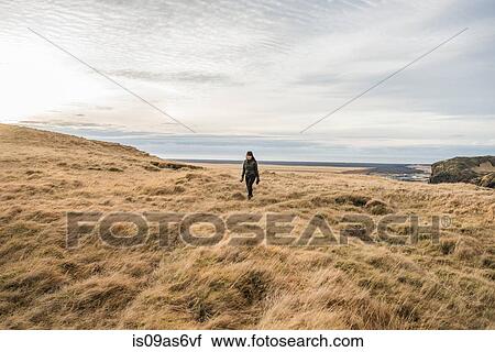 Stock Image - Female tourist walking across moorland, Skogafoss, Iceland. Fotosearch