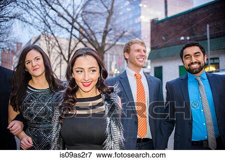 Stock Photo - Four young adult friends on night out walking along street. Fotosearch