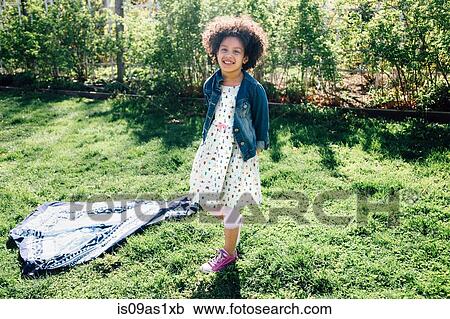 Stock Image - Full length front view of girl standing with hands behind back, looking at camera, smiling. Fotosearch