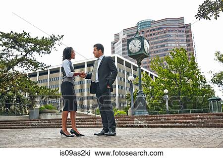 Stock Image - Full length side view of business people shaking hands. Fotosearch